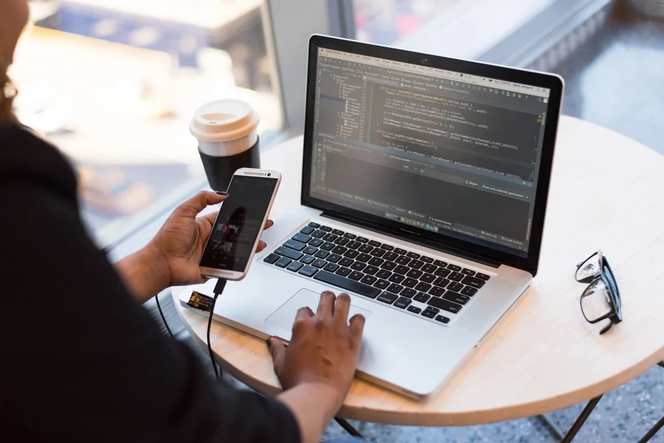 Hands using a laptop with code open at a table